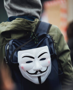 Man wearing a backpack with a Guy Fawkes mask attached